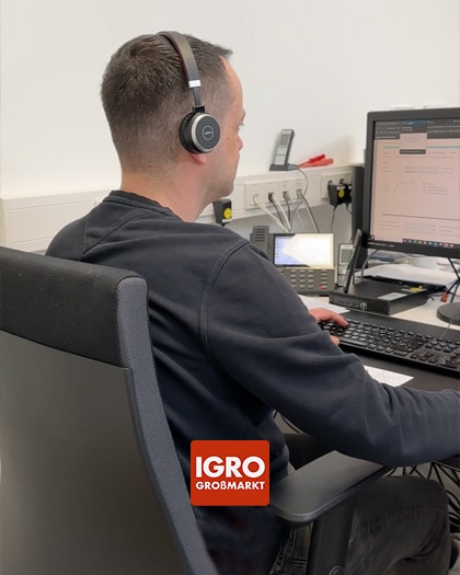 Mitarbeiter im IGRO Innendienst mit Headset am Computer-Arbeitsplatz während der Kundenberatung. Im Vordergrund ist das IGRO GROSSMARKT Logo zu sehen.