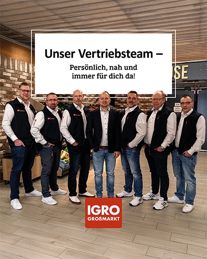 Gruppenfoto von sieben lächelnden Ansprechpartnern des IGRO Vertriebsteams. Sie stehen in einem hellen Großmarkt-Innenraum vor Regalen mit frischem Obst und Gemüse. Die Männer tragen professionelle Arbeitskleidung (weiße Hemden und schwarze Westen) mit Firmenlogos. Oben ist ein weißer, gerahmter Textblock platziert: 'Unser Vertriebsteam – Persönlich, nah und immer für dich da!'. Unten in der Mitte befindet sich das rote IGRO Großmarkt Logo.